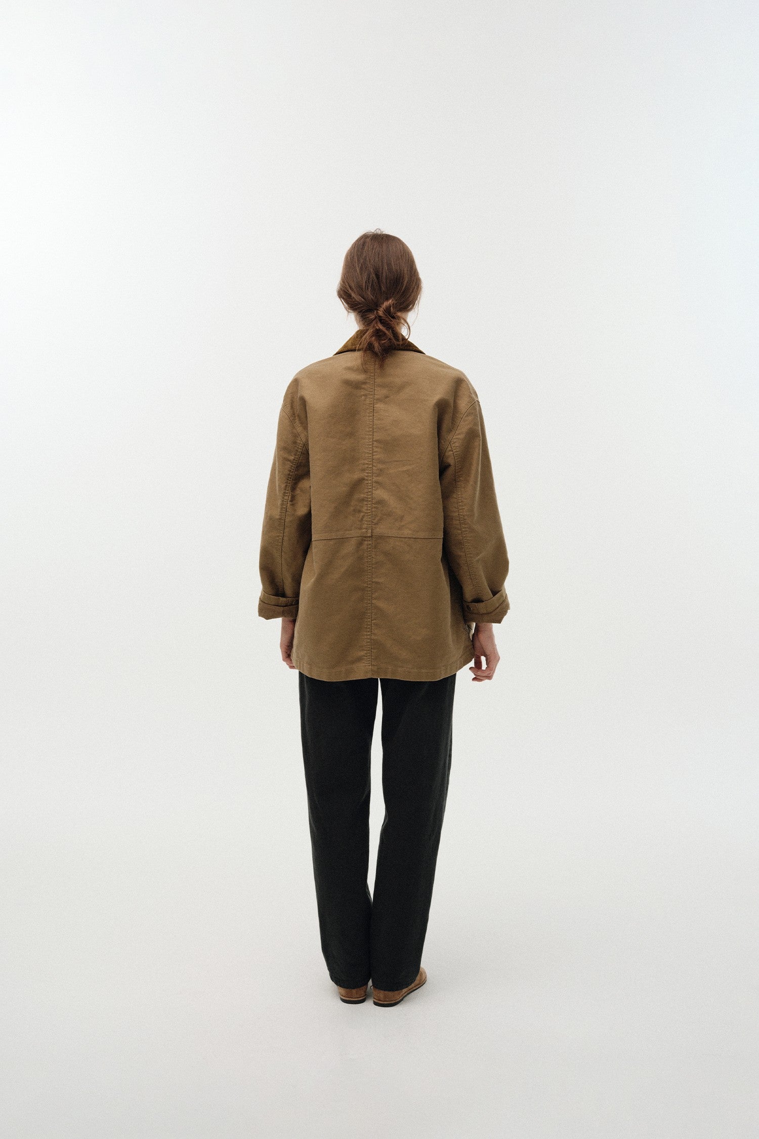 Person wearing a brown jacket and black pants on a white background