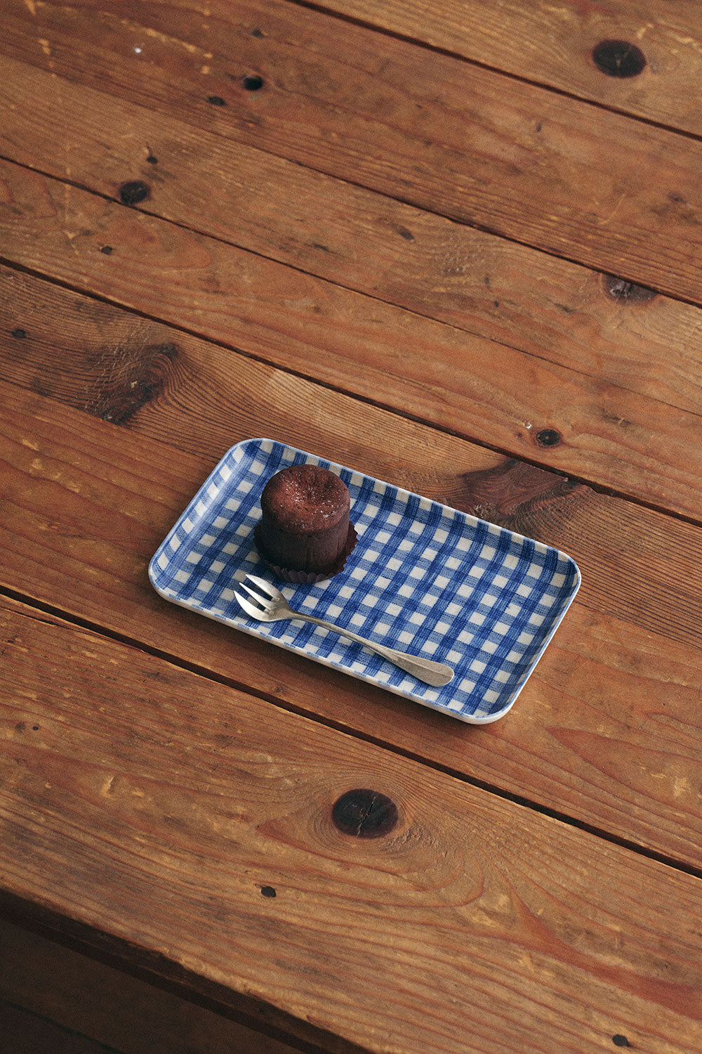 Linen tray with a brownie and fork on a rustic wooden table, featuring a blue gingham pattern.